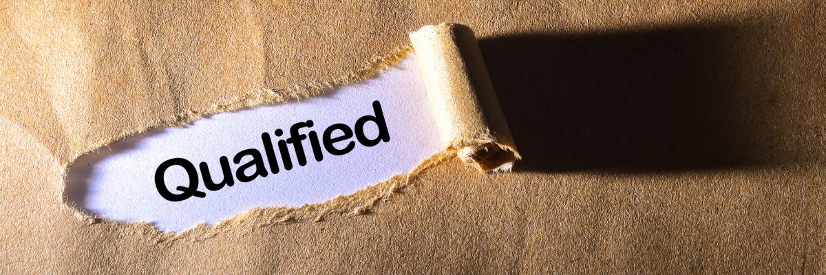 The word "Qualified" revealed through a torn opening in brown craft paper.