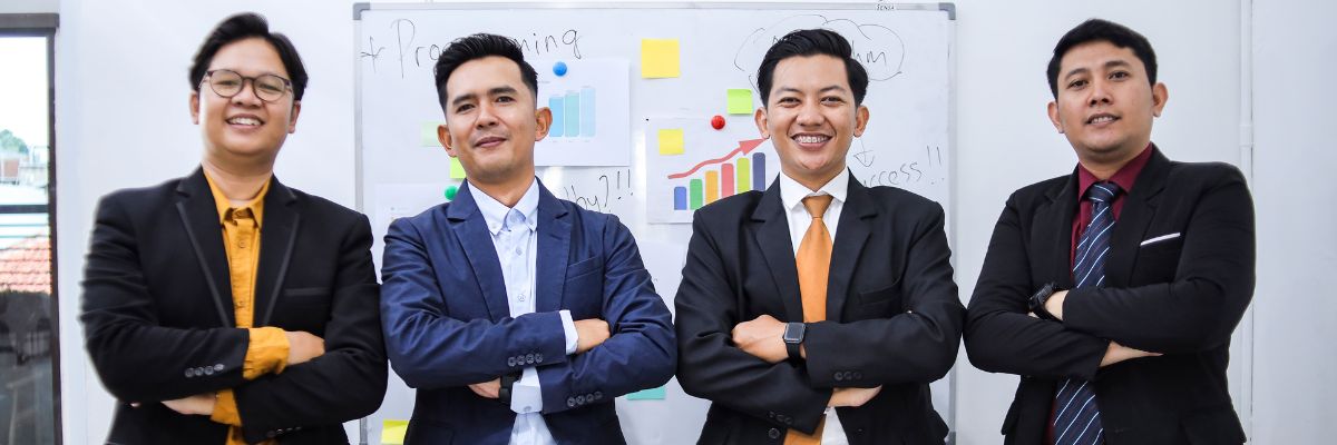 Four men in suits standing with arms crossed in front of a whiteboard.
